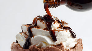Chocolate sauce being poured over whipped cream on a dessert