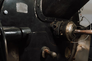 Close-up of a vintage black metal machine with a silver brand plate, a metal coupling component, and a wooden handle on a dark surface.